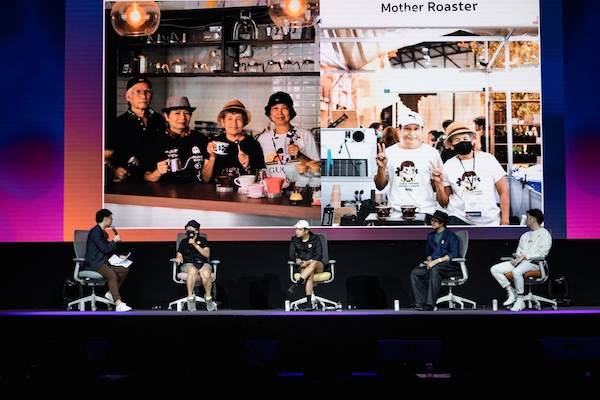 Five people sit on stage with photos of a coffeeshop behind them.